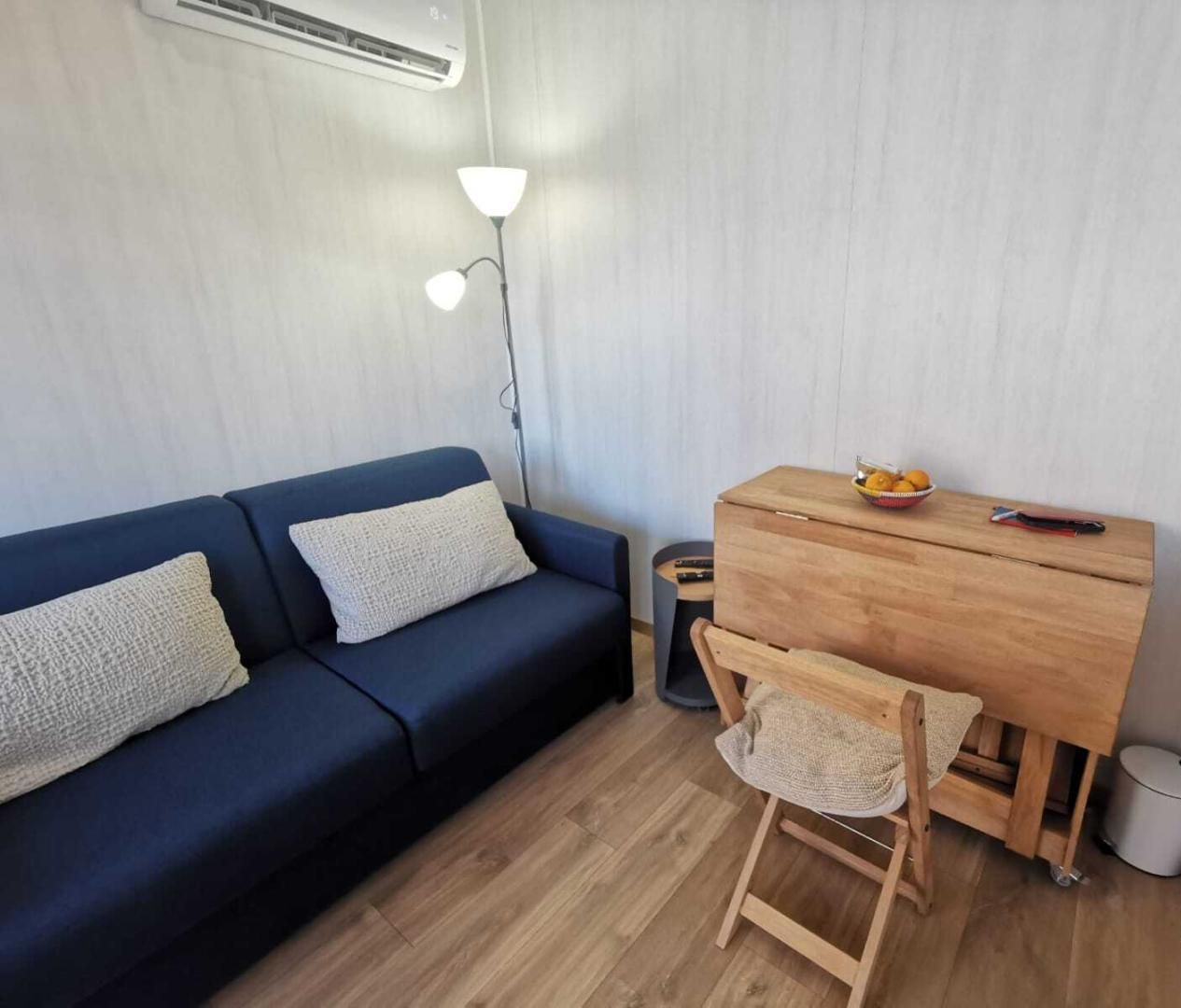 Une petite pièce moderne, avec un canapé bleu foncé, un bureau en bois, une petite chaise et une lampe.