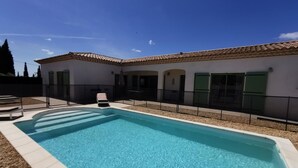 Una piscina rectangular con agua azul cristalina, rodeada por una solana blanca y una valla negra.