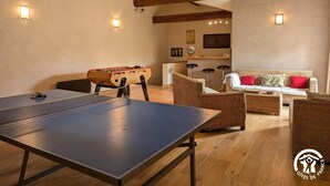 Een kamer met een tafeltennistafel, een tafelvoetbaltafel, rieten meubels en een bar.