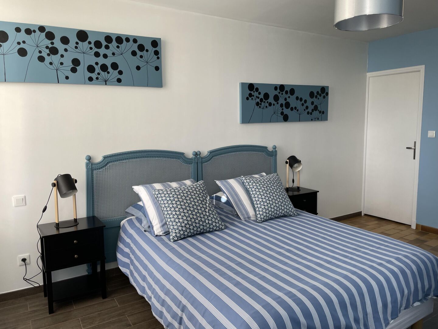 A bedroom with a bed, two bedside tables, a lamp, and artwork on the walls.