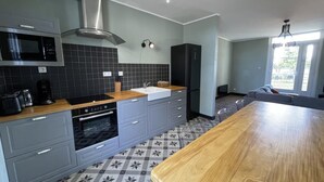 A modern kitchen with grey cabinets, a wooden countertop, a built-in oven, a microwave, and a stainless steel range hood. - Côté Cour - MARAUSSAN - Gîte (MARAUSSAN)