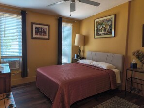A hotel room with a bed, a nightstand with a lamp, a painting on the wall, and a window with blinds. - Inn The Sky Main House Sleeps 8 Firepit (High Rolls)