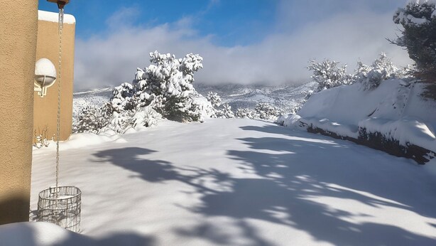 Paesaggio innevato con cielo sereno, un edificio con tetto imbiancato dalla neve e una recinzione metallica.