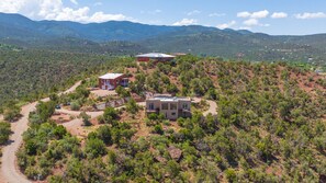 Una zona montañosa y aislada con una amplia casa moderna rodeada de vegetación densa y un camino de tierra.