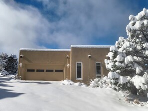 Un edificio de dos pisos con garaje, rodeado de nieve y árboles.