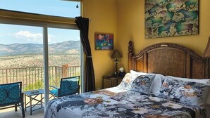 Una camera da letto con un letto, un quadro, una lampada e vista sulle montagne da un balcone.