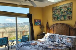 Un dormitorio con cama, un cuadro, una lámpara y vistas a las montañas desde un balcón.