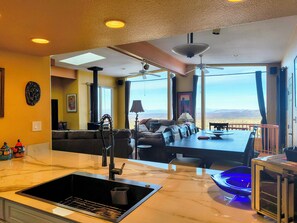 Una cocina moderna con una isla grande, un comedor con vistas y una sala de estar con sofá y lámpara.