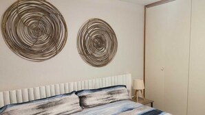 A bedroom with a bed, two wall art pieces, a bedside table with a lamp, and a wardrobe.