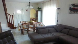 A living room with a sofa, a chair, and a coffee table. There is a dining area with a table and chairs in the background.