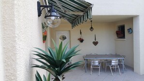 An outdoor patio with a table and chairs, a hanging light fixture, and a potted plant.