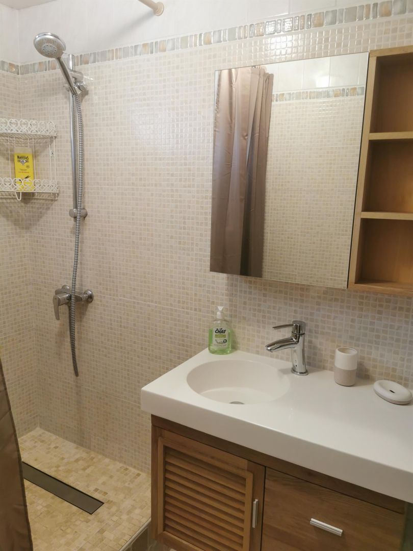 A bathroom with a shower, a sink, a mirror, and a wooden cabinet.