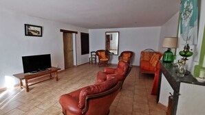Ein Wohnzimmer mit einer Ledersofa, einem Fernseher auf einem Holztisch und einer grünen Lampe auf einem Beistelltisch.