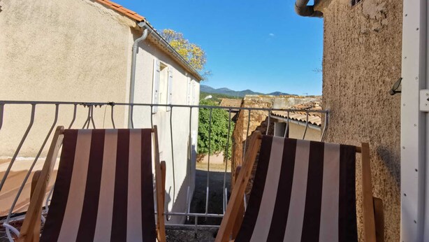Ein Innenhof mit zwei gestreiften Liegestühlen, einem weißen Gebäude und Blick auf ferne Hügel unter blauem Himmel.