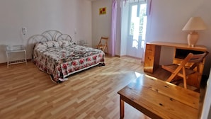 Ein Schlafzimmer mit Bett, Schreibtisch, Stuhl, Lampe und einem fenster mit Vorhängen.