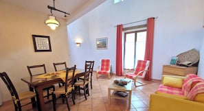 Uma área de refeições com mesa e cadeiras de madeira, um sofá e uma janela com cortinas.
