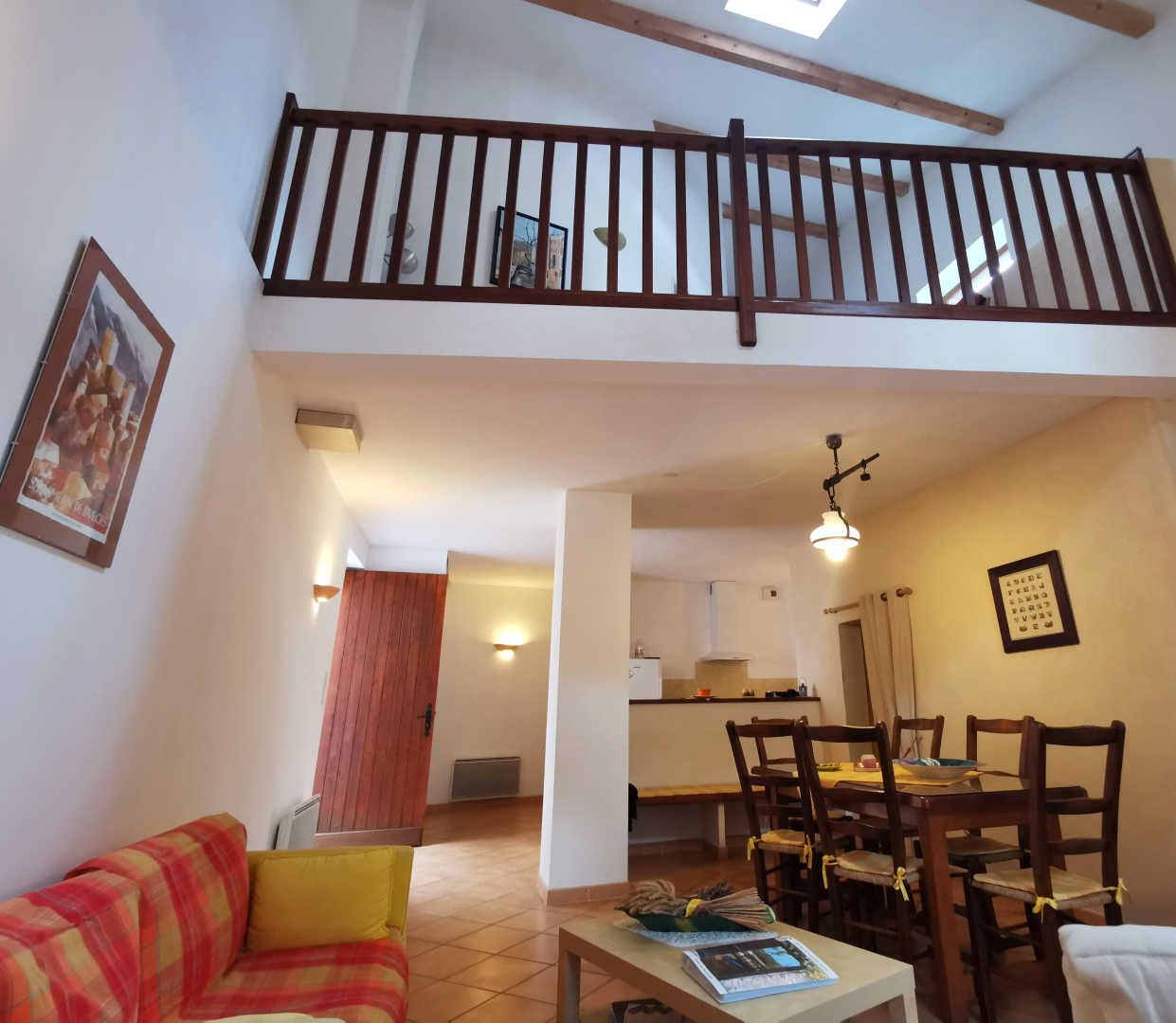 Un vaste espace de vie doté d’un haut plafond, d’un escalier en bois, d’une table à manger avec des chaises et d’une cuisine située au fond de la pièce.