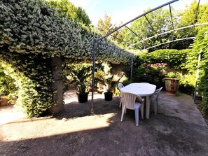 Un patio al aire libre con una mesa y sillas, rodeado de exuberante follaje y plantas florecientes.