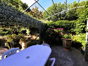 Un patio con mesa blanca, plantas en macetas y una estructura de pérgola de metal.
