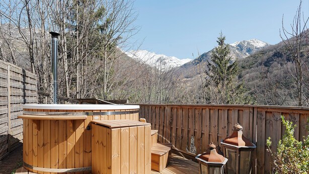 A wooden deck with a hot tub, outdoor lighting, and a view of snow-capped mountains.