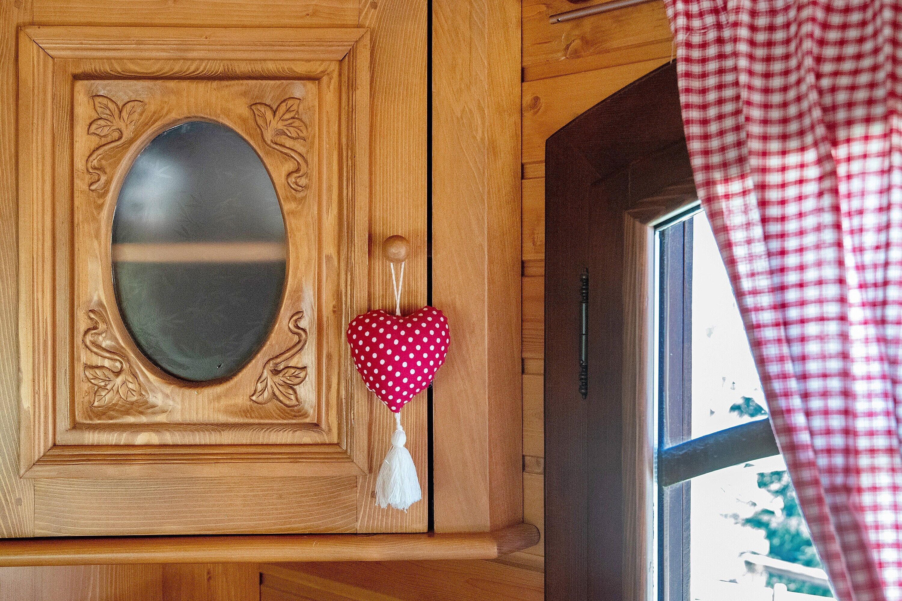 A wooden door with an oval mirror, a heart-shaped decoration, and a window with a checkered curtain.