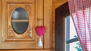 A wooden door with an oval mirror, a heart-shaped decoration, and a window with a checkered curtain.