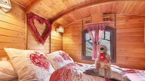 A cozy wooden cabin room with a bed, heart-shaped wall decoration, and a teddy bear.