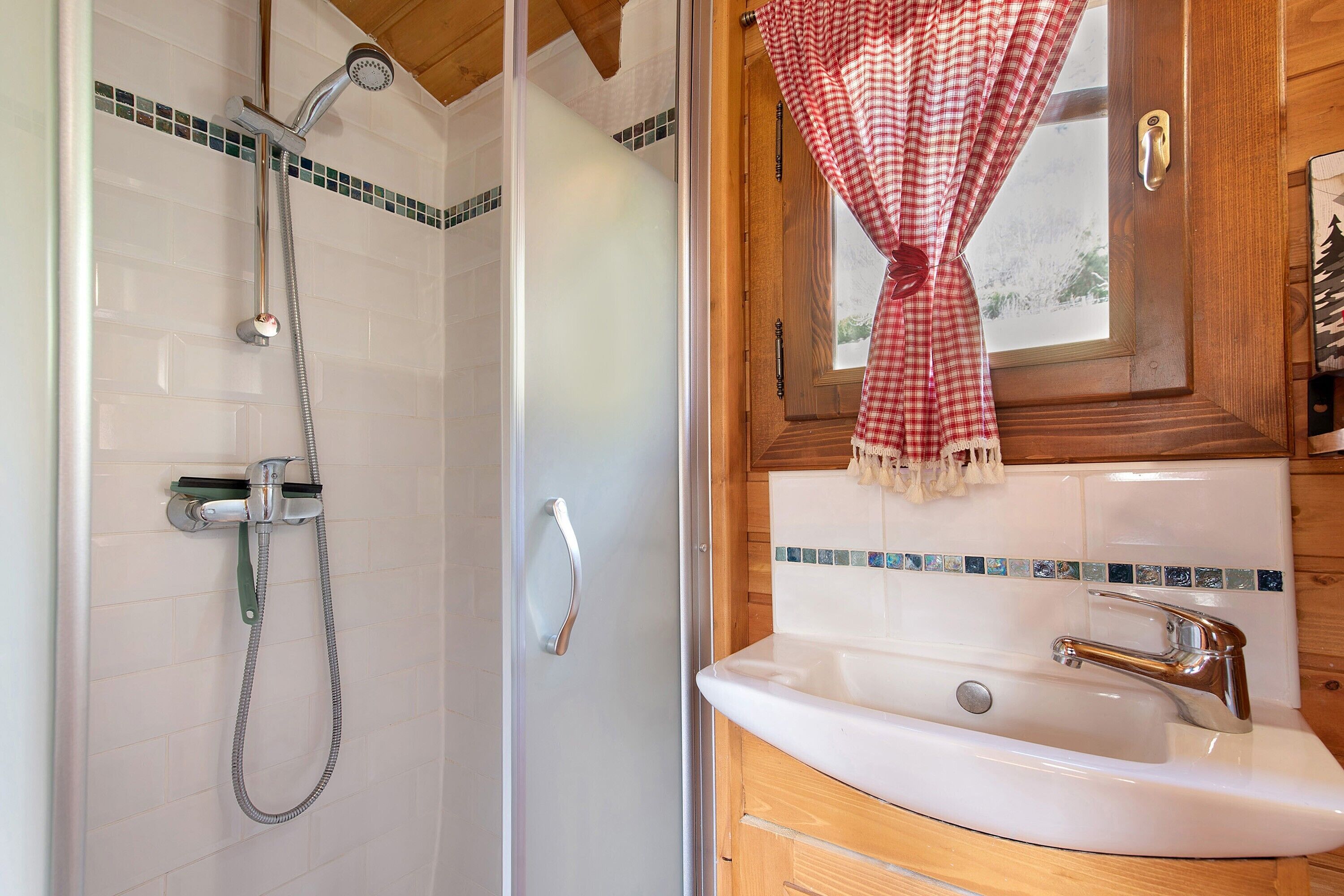 Un bagno con doccia, lavandino e una finestra con tende.