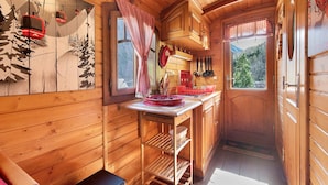 A wooden interior with a kitchen area, wooden cabinets, a window with a view of trees, and a red and white checkered curtain.
