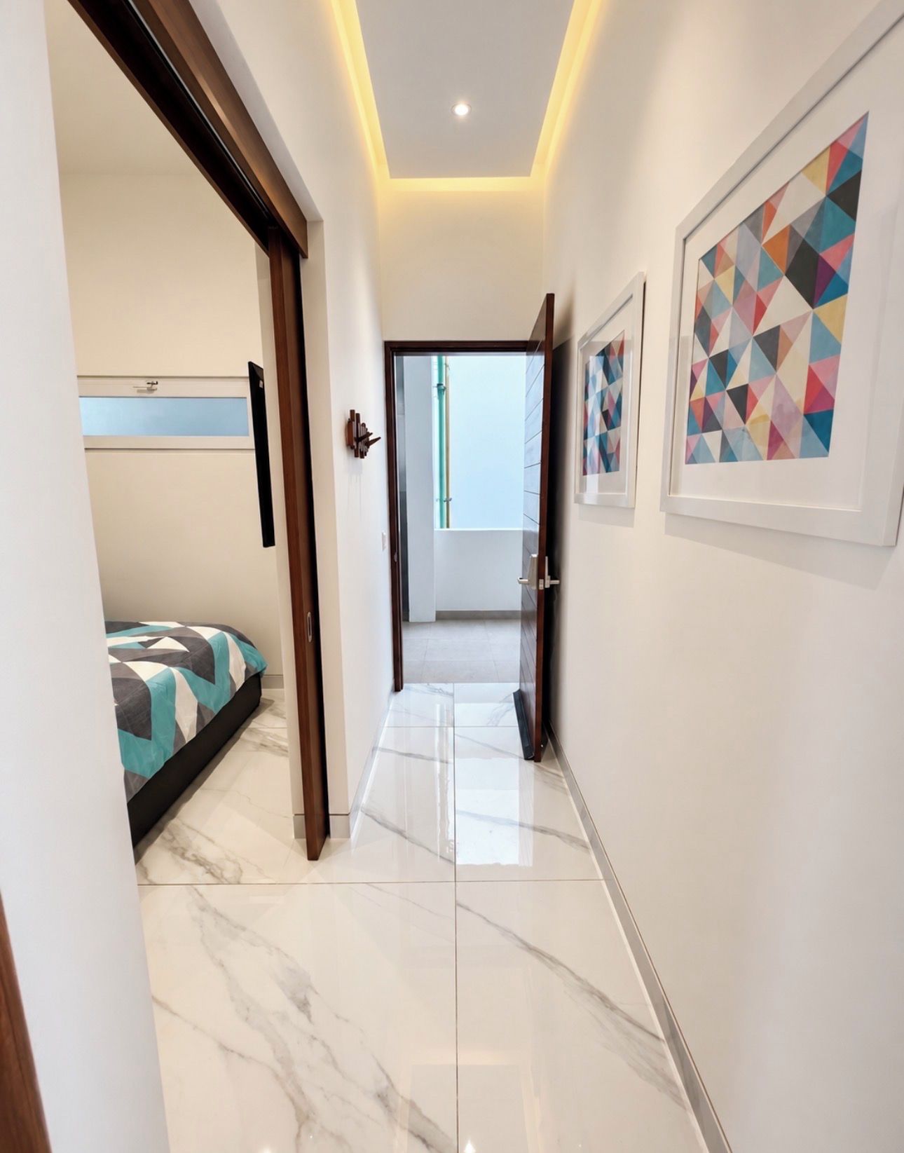 A hallway with a bed, a door, and framed artwork on the wall.