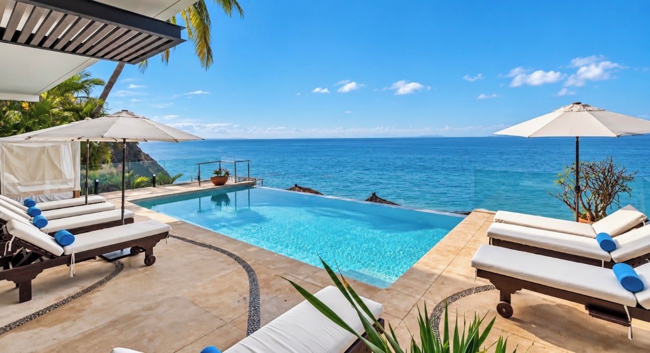 A poolside area with lounge chairs and umbrellas, overlooking a clear blue sea.