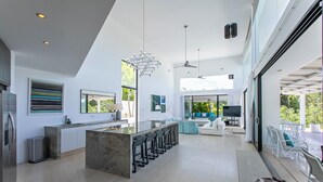 A modern kitchen with a central island, bar stools, and a dining area with white furniture. - Atelier House  (Weston)