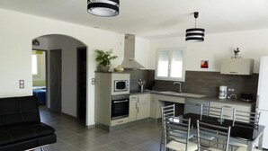 A modern kitchen with a central island, built-in oven, microwave, and a dining area with a black sofa and metal chairs. - La Celestine - PORTEL DES CORBIERES (PORTEL DES CORBIERES)