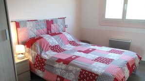 A neatly made bed with a patchwork quilt, a bedside table with a lamp, and a window with blinds. - La Celestine - PORTEL DES CORBIERES (PORTEL DES CORBIERES)
