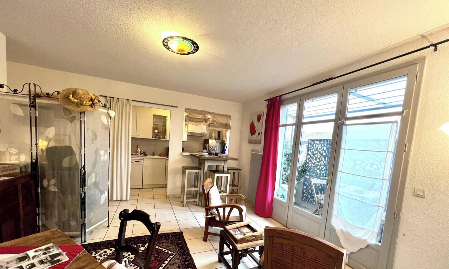 A room with a dining area, kitchen, and a large window with curtains.