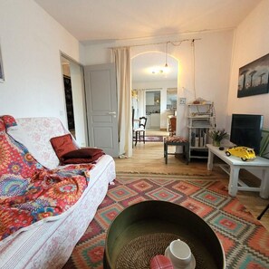 Una sala de estar acogedora con un sofá, una mesa de centro y un televisor. Se observa una cocina al fondo.