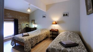 Ein Zimmer mit zwei Einzelbetten, einem Schreibtisch, einem Stuhl, einer Lampe und einem Fenster mit Vorhängen.