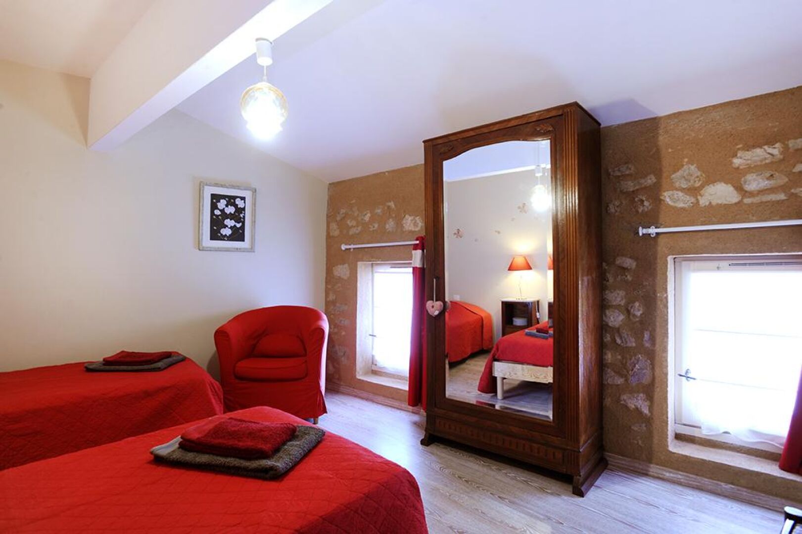 Una habitación con dos camas, una silla roja, un armario de madera y un espejo grande.