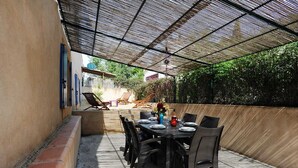 Eine Terrassesitzgruppe im Freien mit Tisch und Stühlen, umgeben von einem überdachten Bereich mit Mesh-Dach.