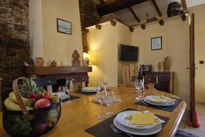 Un coin repas avec une table en bois dressée pour le repas, un panier de fruits et des verres à vin.