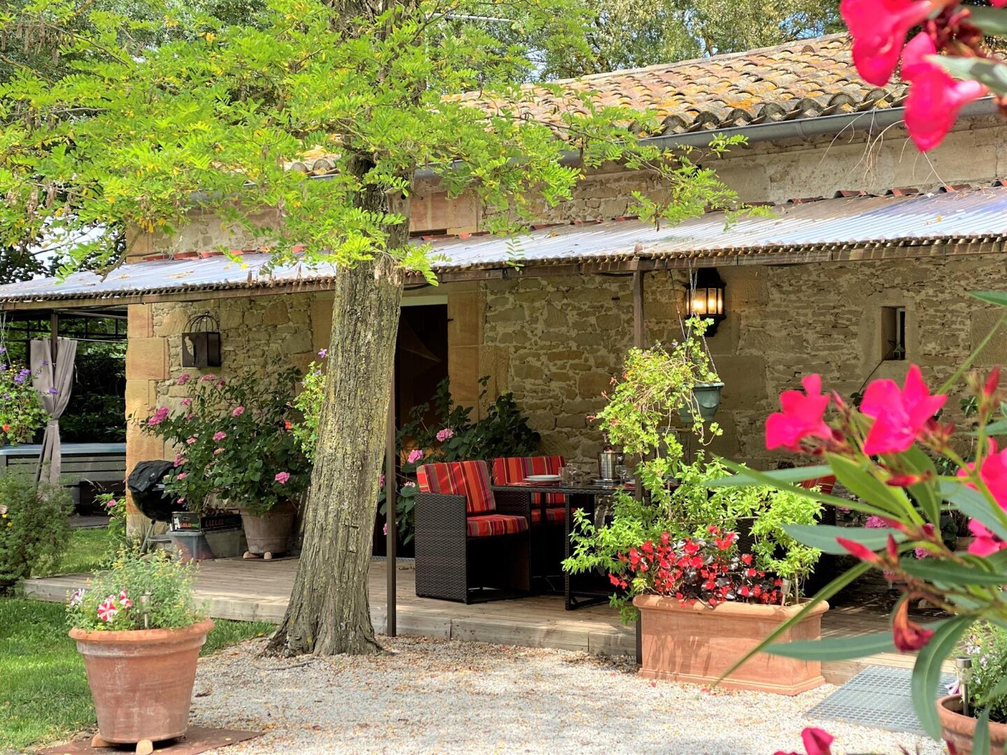 A stone building with a tiled roof, a covered patio with outdoor seating, and potted plants.