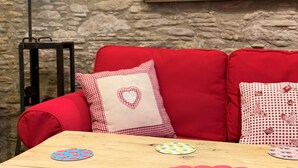 Un sofá rojo con almohadones cuadriculados, una mesa de madera con posavasos, una lámpara y una pared de piedra.