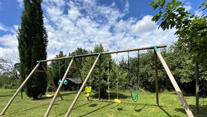 Un columpio de madera con dos asientos, un área de juego con red y un patio cubierto de césped.