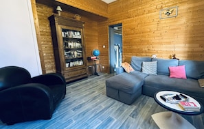 Una sala de estar acogedora con un sofá seccional gris, un sillón negro, una estantería de madera y una mesa de centro redonda con revistas y un globo terráqueo.