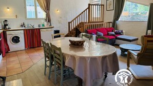 A cozy living area with a round dining table, a sofa, and a staircase leading to an upper level. - Au Pied du Château - PADERN (PADERN)