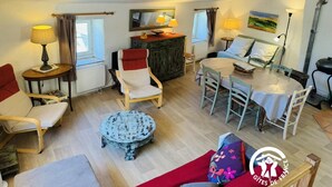 A cozy living room with a wooden ceiling, a dining table, a red sofa, and a small round table with a lamp. - Au Pied du Château - PADERN (PADERN)