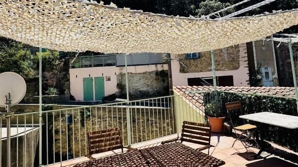 An outdoor patio with a patterned table and chairs, a pergola, and a view of rocky terrain and trees. - Au Pied du Château - PADERN (PADERN)