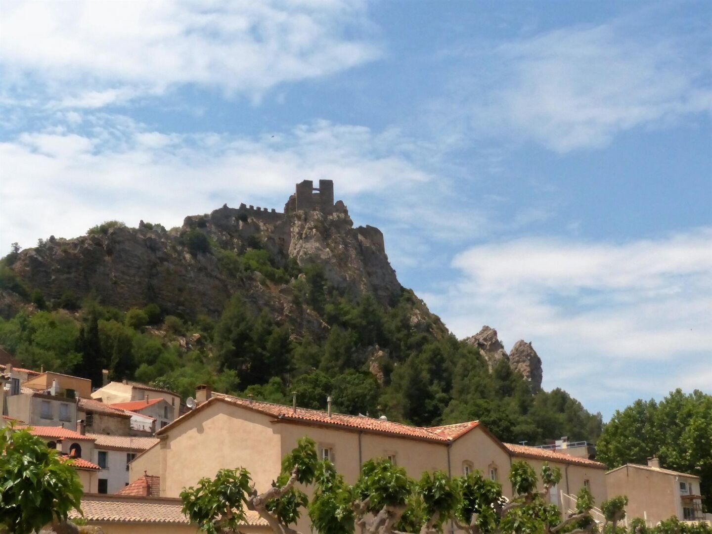 Un pueblo costero con una colina rocosa destacada y las ruinas de un castillo histórico.