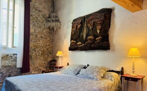 A bedroom with a stone wall, a bed with patterned bedding, two bedside tables with lamps, and a rustic artwork above the bed.