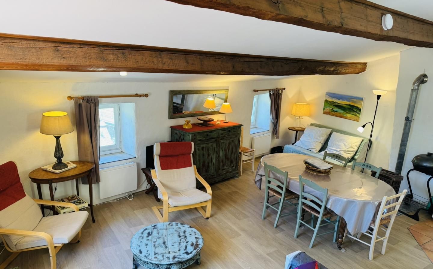 A cozy living room with a wooden ceiling, a dining table, a red sofa, and a small round table with a lamp.